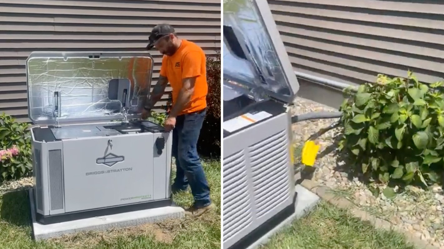 A person interacts with an open generator located on a concrete slab near shrubs.