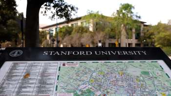 A campus map displaying Stanford University with directional information and a nearby building in the background.