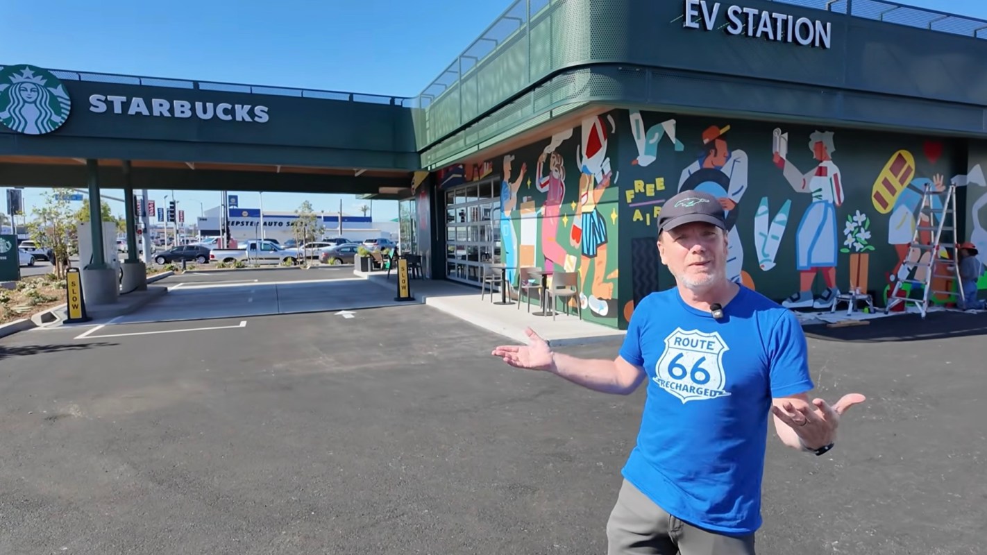 A man stands in front of a Starbucks with a colorful mural and an EV station sign.
