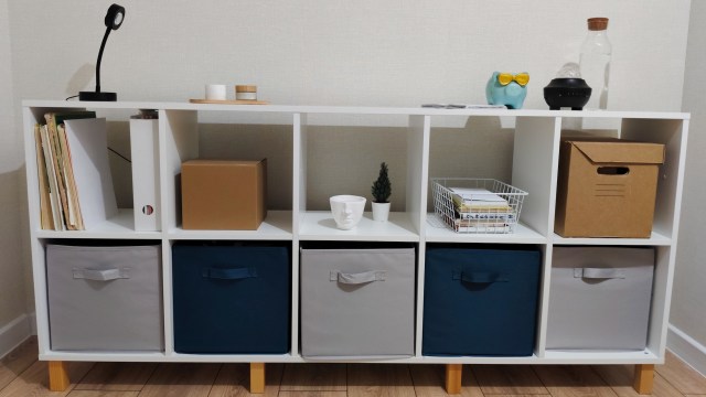 A white shelving unit with storage boxes, books, a small plant, and decorative items.