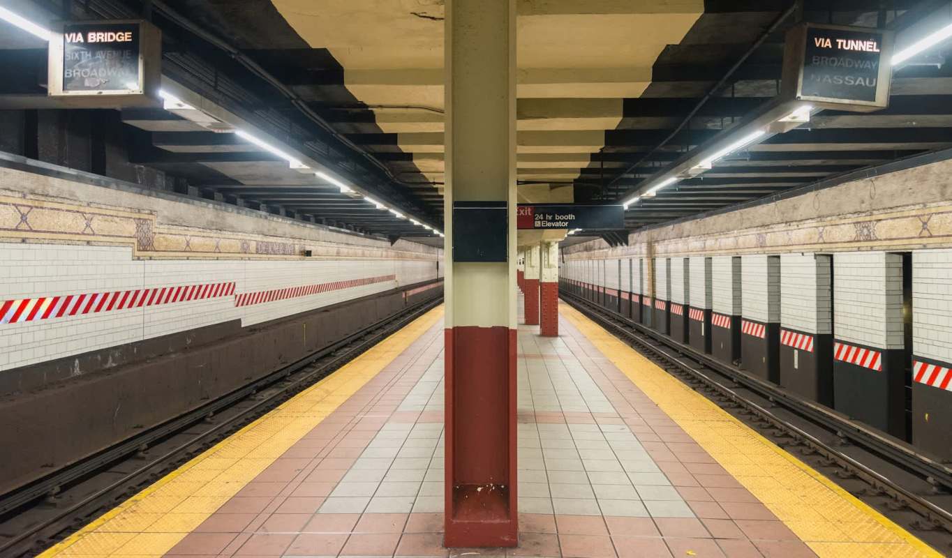 A subway station platform with tiled walls, yellow safety markings, and signs for train directions.