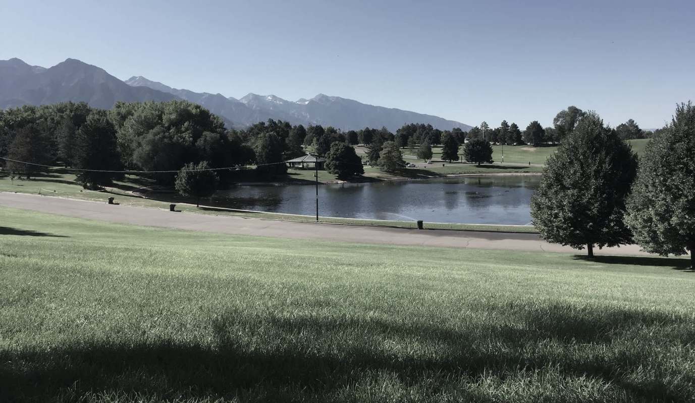 A park with a pond surrounded by trees and mountains in the background.