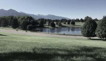 A park with a pond surrounded by trees and mountains in the background.