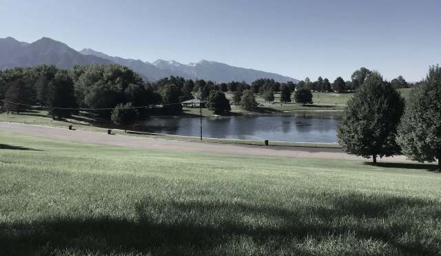 A park with a pond surrounded by trees and mountains in the background.