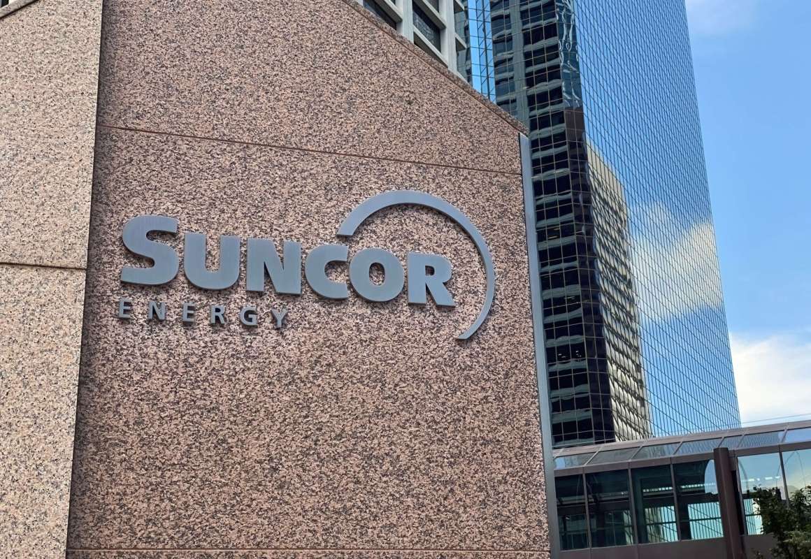 Suncor Energy sign on a textured wall with modern buildings in the background.
