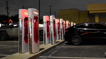 Several Tesla charging stations are illuminated at night, lined up next to a parked black car.