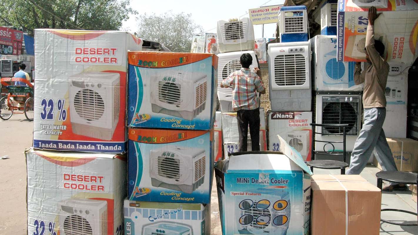 A vendor arranges stacked boxes of desert coolers and room coolers in an outdoor market.