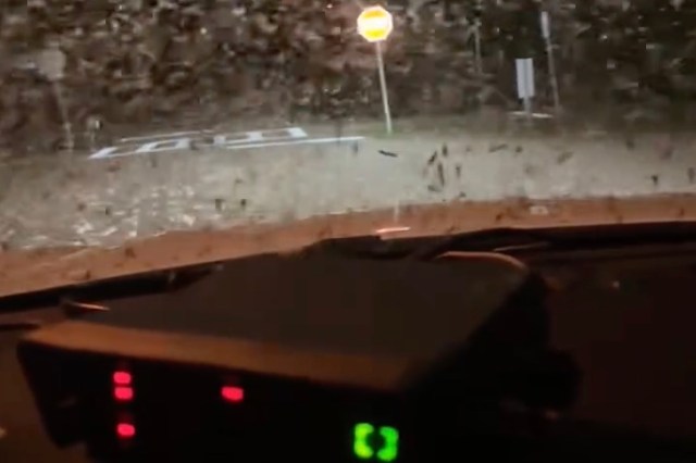 A view from inside a vehicle with a dashboard display, showing an illuminated stop sign through a dirty windshield.