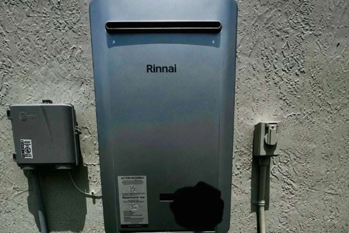 A Rinnai tankless water heater mounted on a textured wall next to a utility box and conduit.