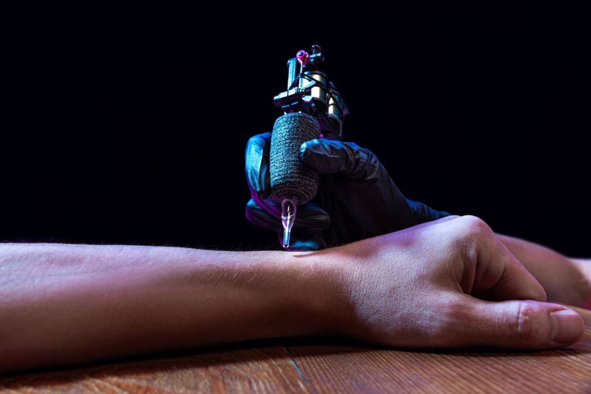 A gloved hand with a tattoo machine against someone's arm.