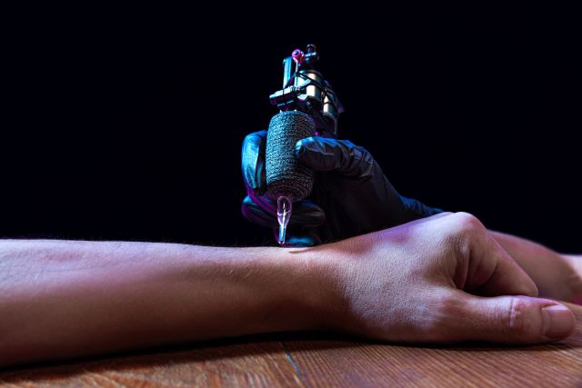 A gloved hand with a tattoo machine against someone's arm.