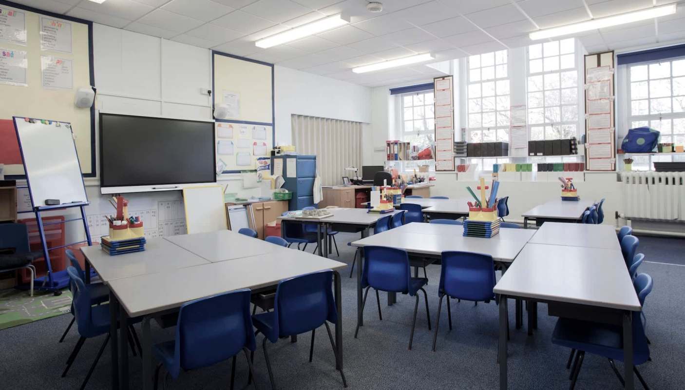 A classroom with desks, chairs, a large screen, and various educational materials on the walls.