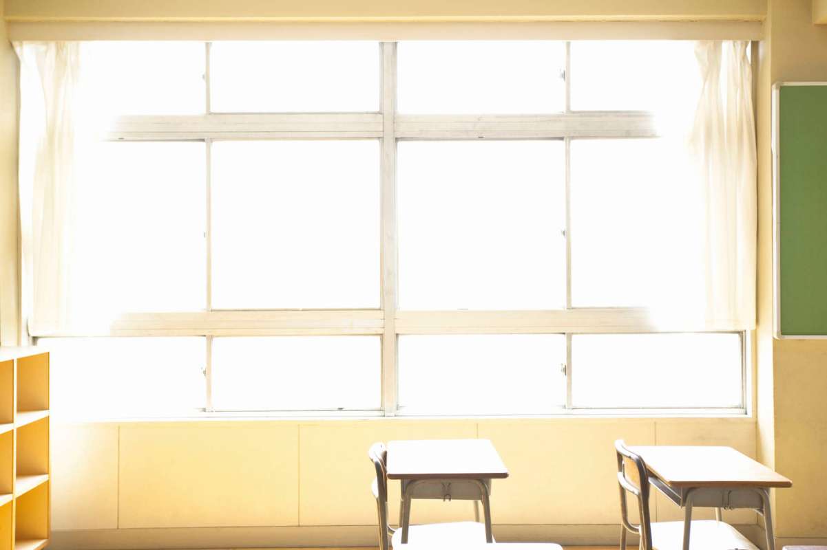 A classroom with empty desks and a bright window with sheer curtains.