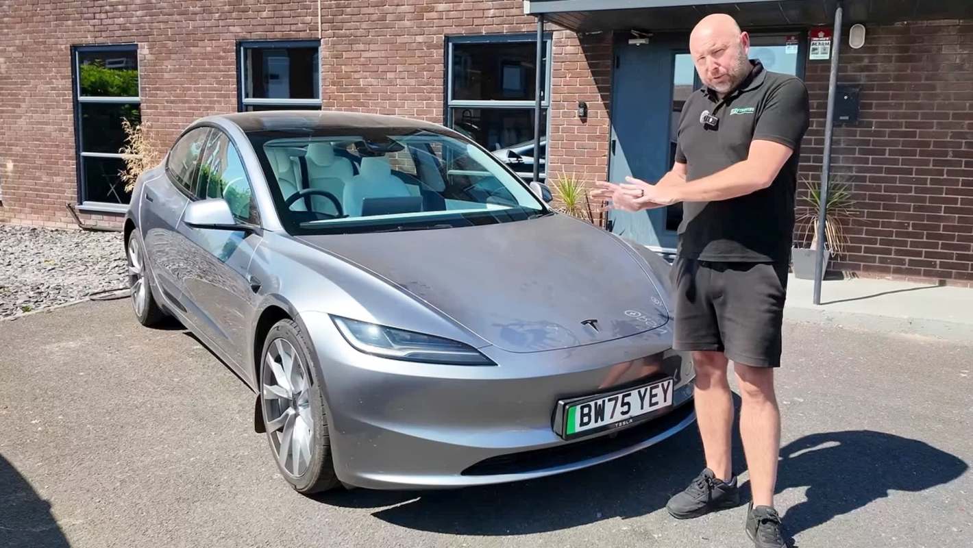 A man gestures toward a silver Tesla parked outside a building.