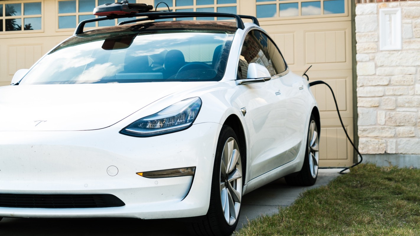 A white electric car is parked and charging near a garage.