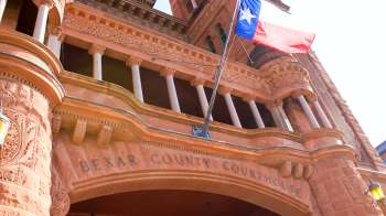 A close-up view of the Bexar County Courthouse facade with an American flag flying.