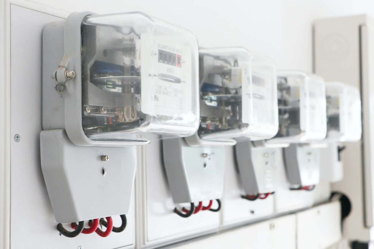 A row of electrical meters mounted on a wall with visible wiring.