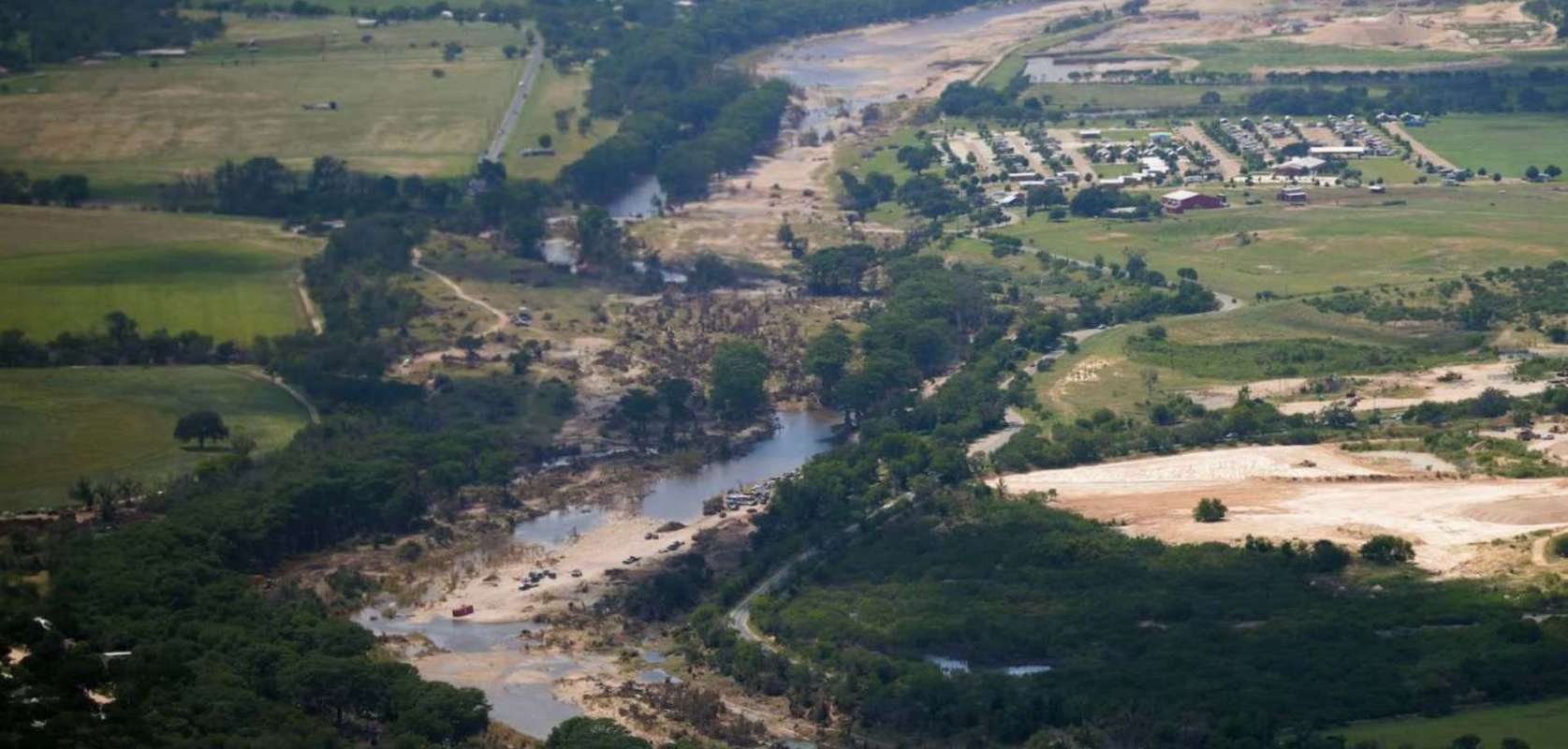 Aerial view of a river winding through a landscape with fields, trees, and residential areas nearby.