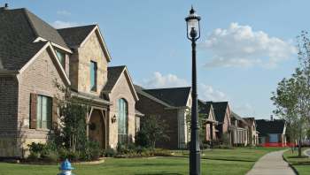 A residential street with several houses, a lamp post, and a landscaped lawn.