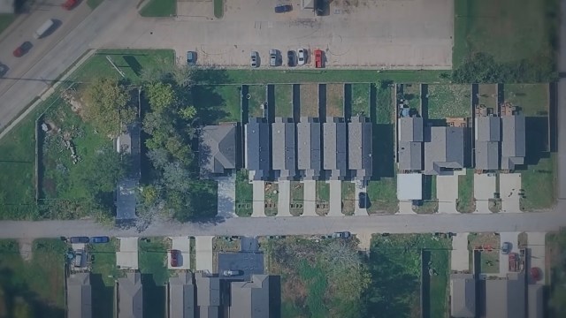 An overhead view of a residential area with houses, parking spaces, and tree-lined streets.