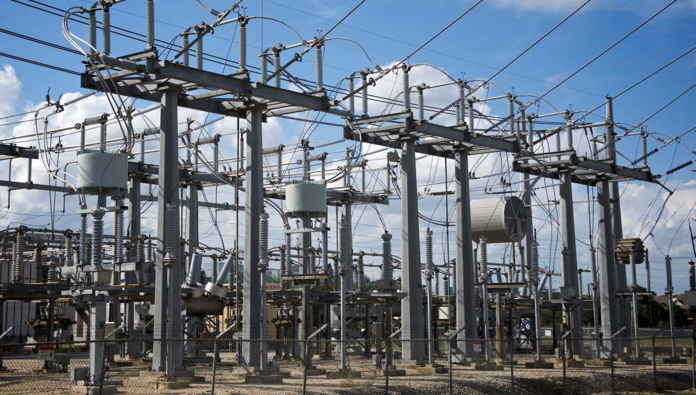 An electrical substation with power lines, transformers, and associated equipment under a blue sky.