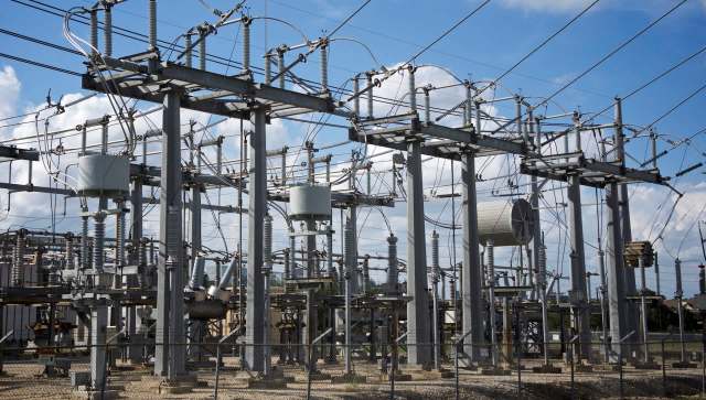 An electrical substation with power lines, transformers, and associated equipment under a blue sky.