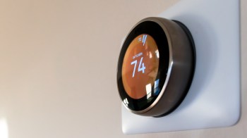 A smart thermostat displaying a temperature of 74 degrees Fahrenheit on a wall.