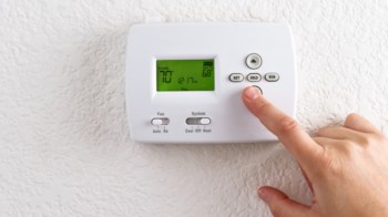 A hand adjusting a digital thermostat displaying a temperature of 70 degrees.