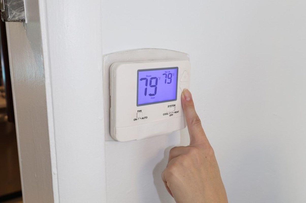 A person adjusts a thermostat displaying a temperature of 79°F.