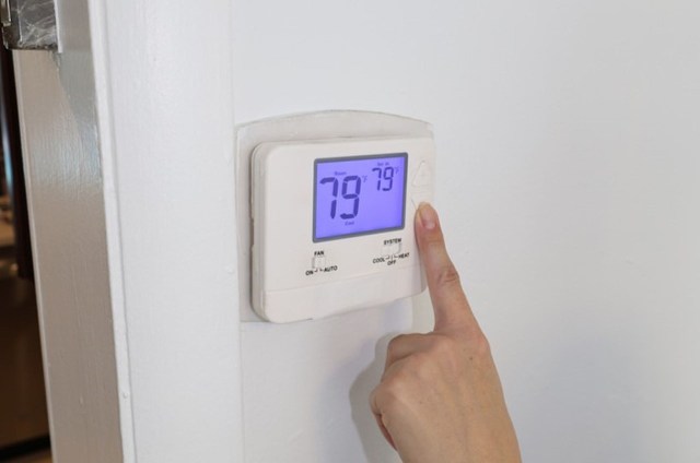 A person adjusts a thermostat displaying a temperature of 79°F.