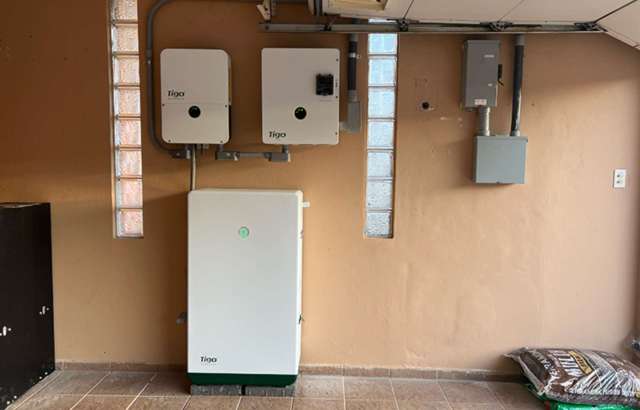Electrical equipment mounted on a wall in a garage, including solar inverters and a battery storage unit.