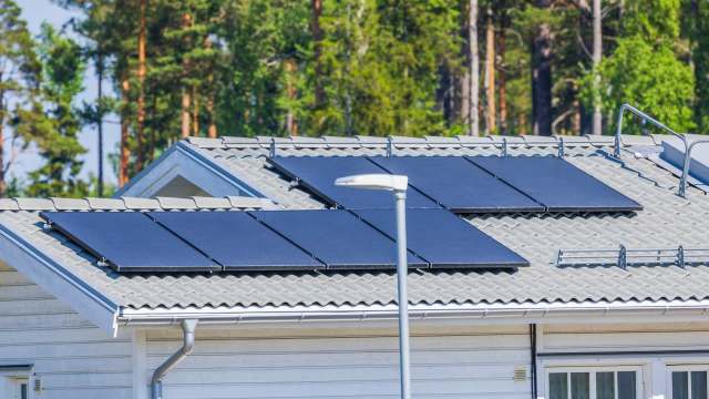 A house with solar panels on the roof and trees in the background.