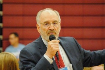 North Dakota senator Tim Mathern speaks into a microphone while gesturing in a gymnasium setting.