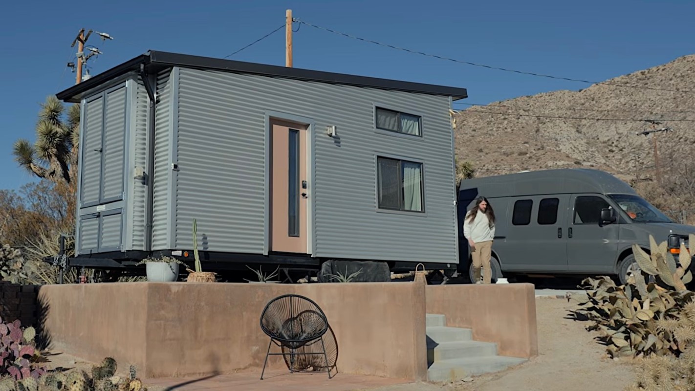 A tiny house with a modern design beside a parked van in a desert landscape.