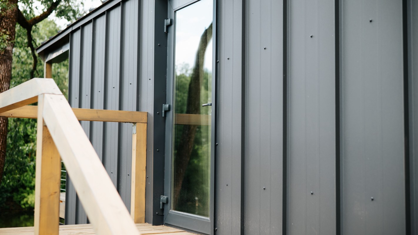 A wooden railing leads to a modern building with a large glass door and gray metal siding.