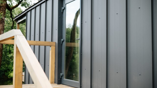 A wooden railing leads to a modern building with a large glass door and gray metal siding.