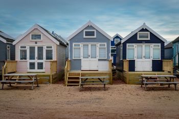 Three tiny homes in pastel colors with wooden steps and picnic tables in front, set against a sandy ground.
