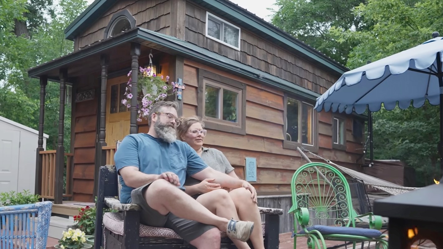 A couple sitting outside their tiny home.