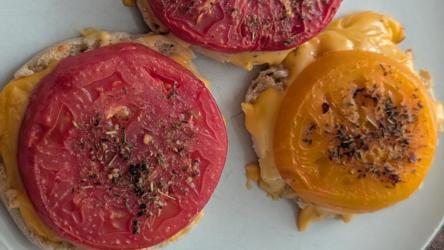 Three toasted English muffins topped with melted cheese and slices of red and yellow tomatoes, seasoned with herbs.