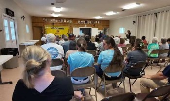 A group of people seated in rows, facing a presentation in a community hall.