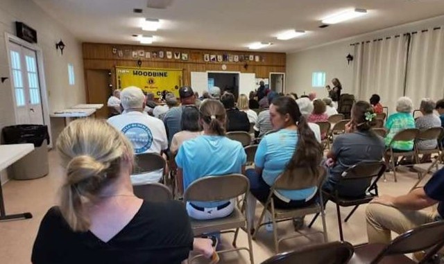 A group of people seated in rows, facing a presentation in a community hall.