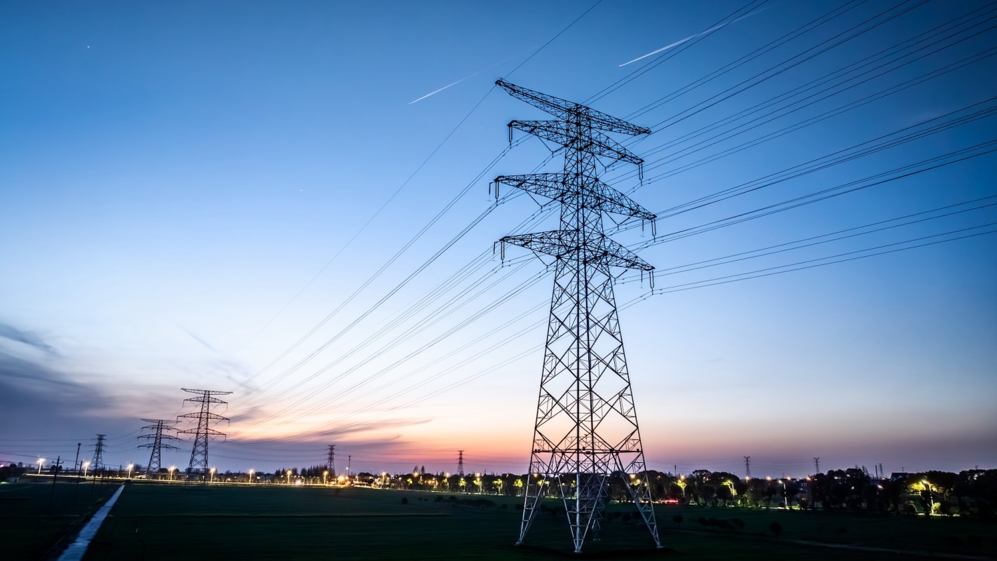 Electricity towers and power lines stand against a twilight sky with scattered clouds.