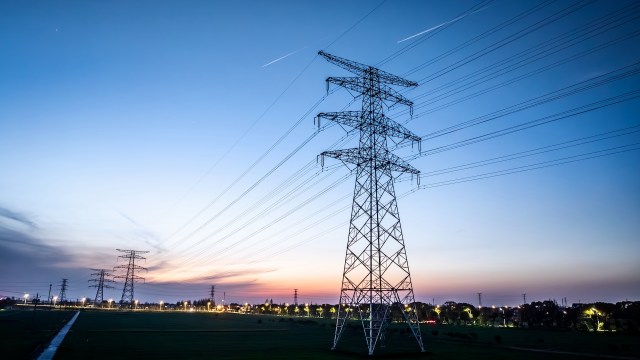 Electricity towers and power lines stand against a twilight sky with scattered clouds.