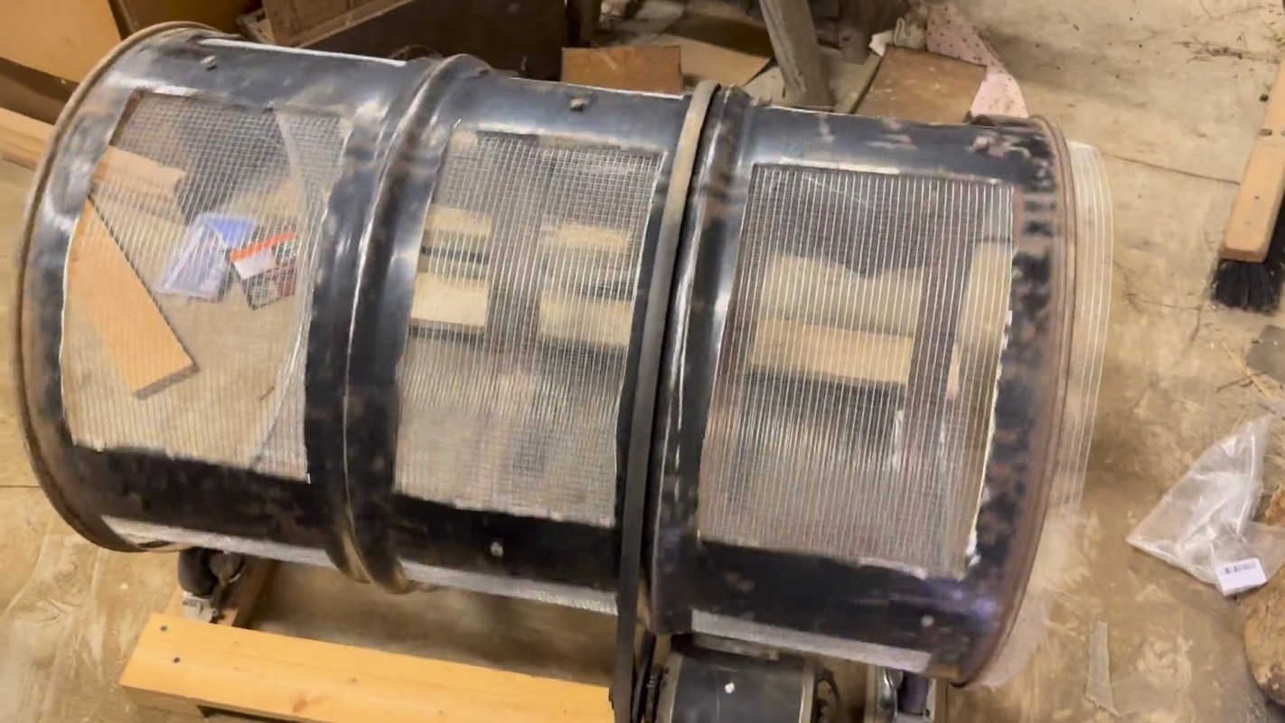 A cylindrical object made of metal and mesh, positioned on a wooden surface in a workshop.