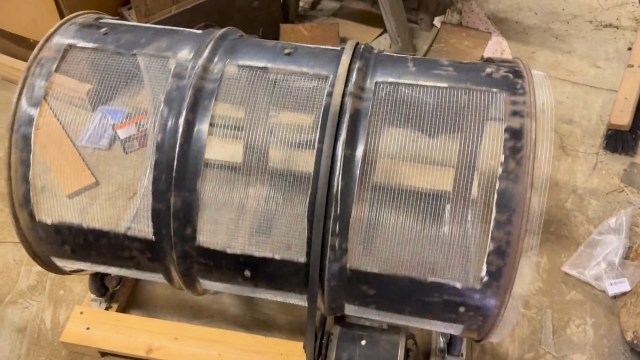 A cylindrical object made of metal and mesh, positioned on a wooden surface in a workshop.