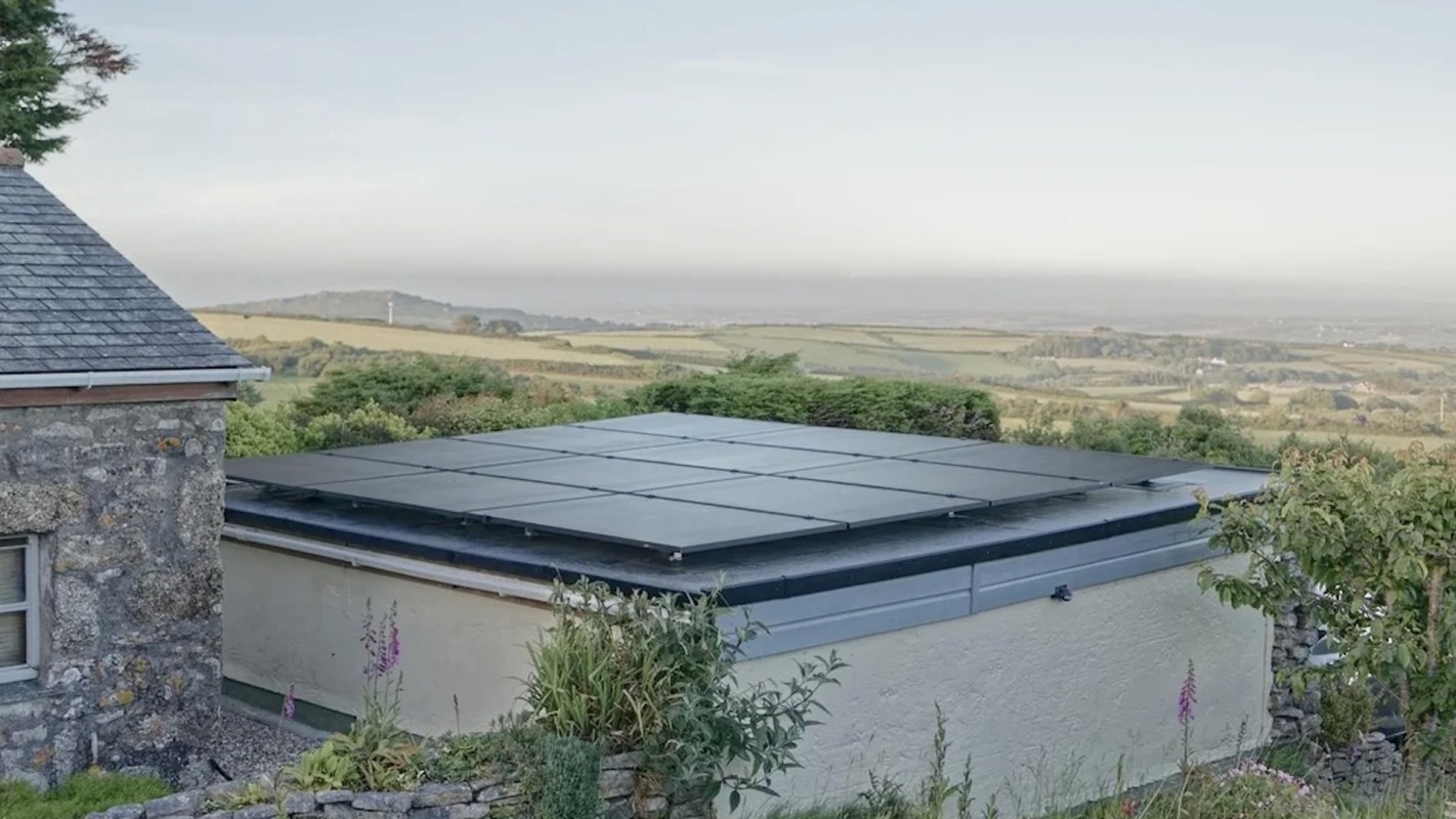 A building with a solar panel roof surrounded by green landscape and hills in the distance.