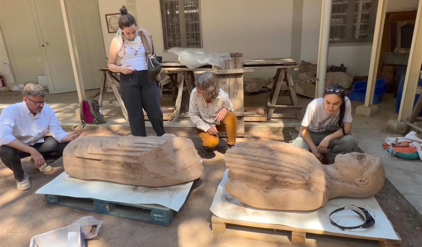 Archaeologists examine two parts of a statue.