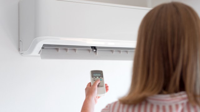 A person holds a remote control aimed at a wall-mounted air conditioning unit.