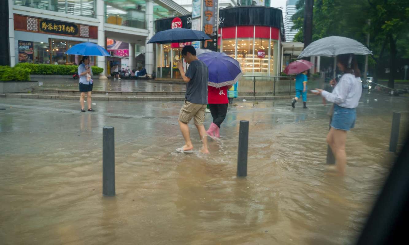 People walk through a flooded street holding umbrellas.