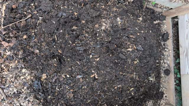 A pile of dark, moist compost containing organic matter and small pieces of wood.